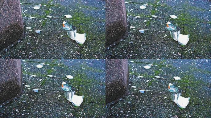 在公共混凝土垃圾箱旁边的人行道上破碎的碎玻璃瓶子碎片