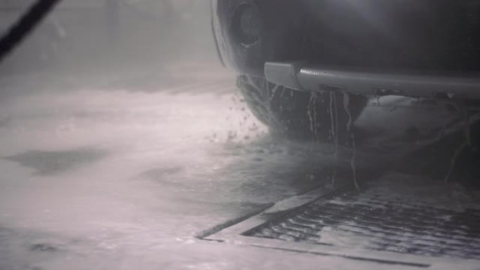 从汽车保险杠上滴下来的带有清洁剂的水。自助室内洗车流程。具有选择性聚焦和慢动作的特写视图。