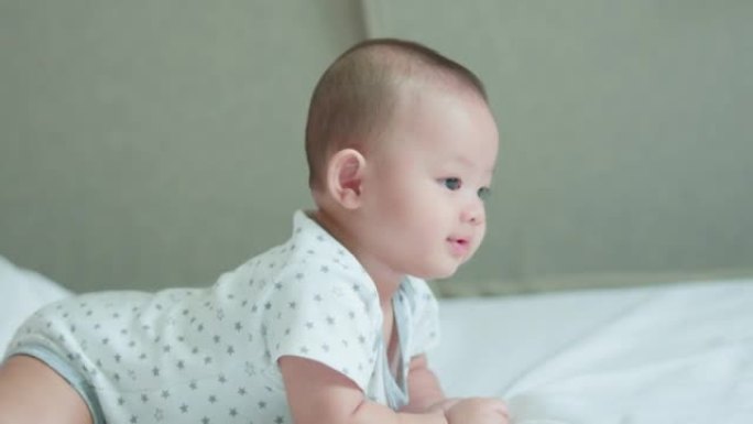 幸福的家庭，可爱的亚洲新生婴儿躺着，爬着在白色的床上嬉戏，笑容满面。天真的小新婴儿可爱。父母身份和母