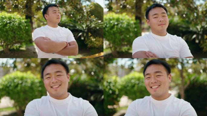 年轻的中国男子微笑着自信地站在公园里双臂交叉手势