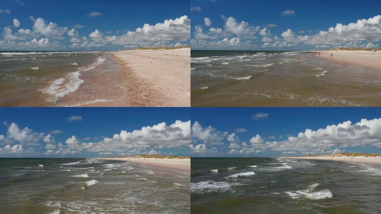 向前飞过海岸。晴天海浪冲刷沙滩。人们在水上享受美好的一天。丹麦