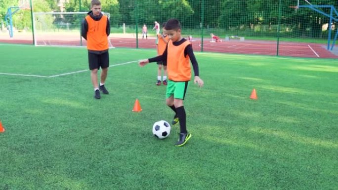 活跃自信的青少年男孩的特写镜头，他们在联合课上与足球教练一起训练在足球场上踢足球，4k