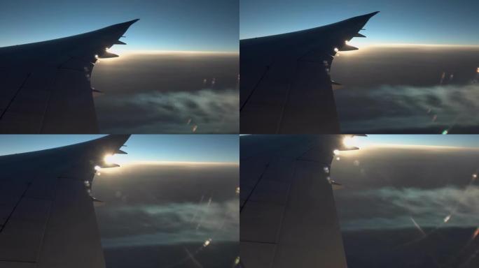 飞机机翼和喷气流从窗户飞行，日落天空，由日落太阳突出显示的喷气流