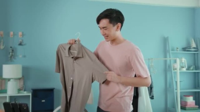 一名亚洲男子在他的商店的智能手机直播前展示衣服。技术在线商业概念。