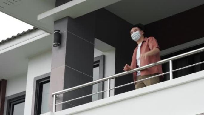 检疫男子戴着口罩，在家里的阳台上与邻居打招呼，下雨，冠状病毒 (新型冠状病毒肺炎) 大流行