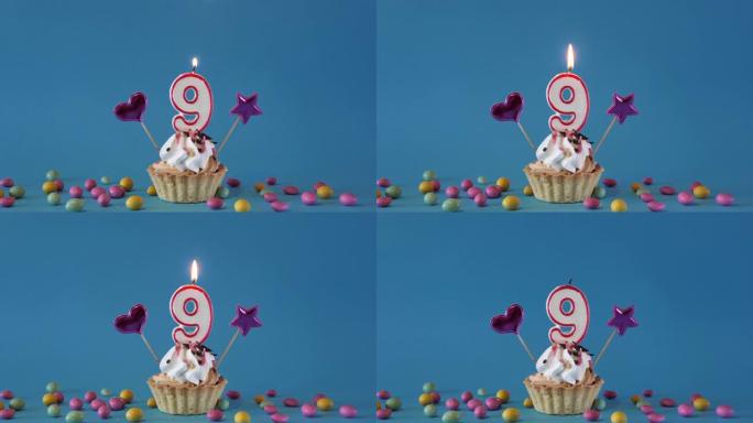 祝9岁的孩子生日快乐，带蜡烛的生日蛋糕和蓝色背景上的生日装饰品。点燃并熄灭纸杯蛋糕上的节日蜡烛