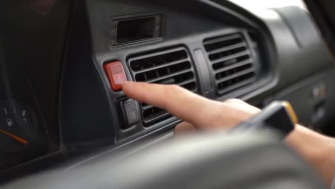 一名男子将手指按在面板上的汽车应急照明按钮上。在路上寻求帮助。车辆故障通知。自动紧急按钮