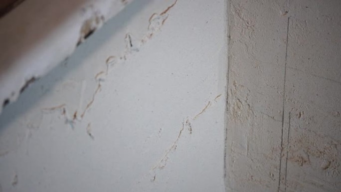 男性建造者使用金属刮铲制作油灰墙，修理工用剥皮膏填充刮铲并覆盖水泥墙面。建筑工人整平墙体和住宅角度改