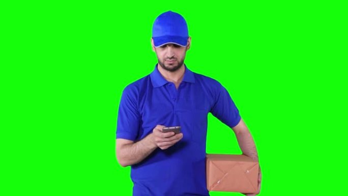 高加索送货员拿着包裹一边用手机穿着蓝色制服在绿屏背景前