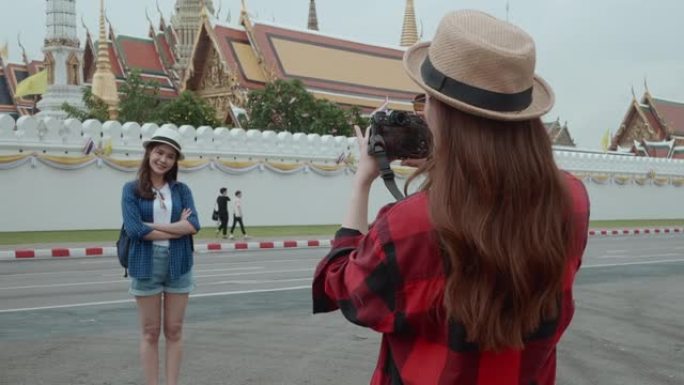 两名美丽的亚洲年轻女子游客拍摄了一张照片，背景是泰国曼谷的大皇宫和Wat Phra Kaew。后视图