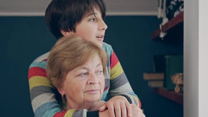 十几岁的孙子将祖母抱在脖子后面，对她说话。