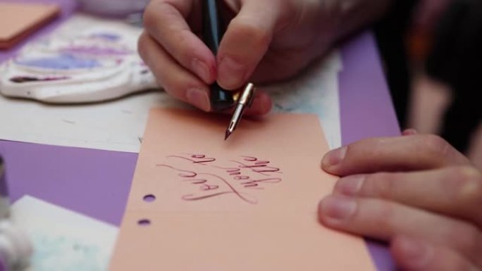 用墨水钢笔羽毛书写书法的过程，书法家在大师班用钢笔和墨水瓶在明信片纸上练习书写，手视图