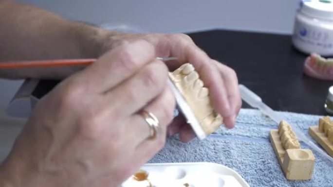 为一个人创造假牙的过程。大师的手上漆并将材料涂到假肢上。男性用刷子在颌骨假体上工作