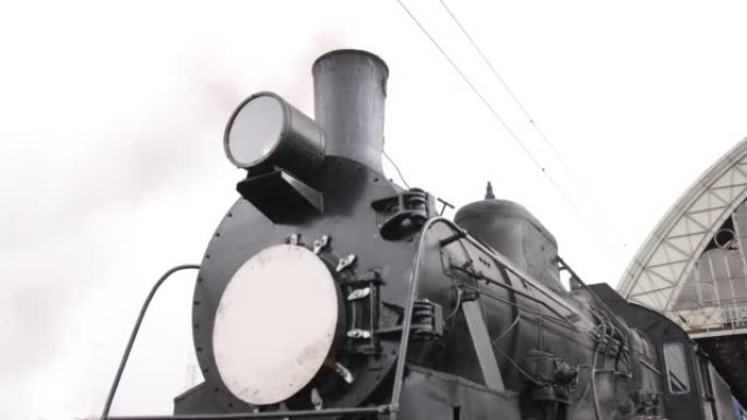 复古蒸汽火车从火车站出发。带蓝色汽车的旧黑色蒸汽火车