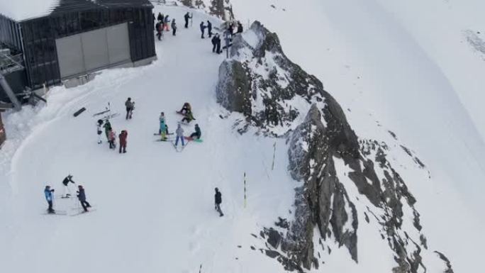 白雪皑皑的滑雪胜地上的人们，在法国高雪维尔阿尔卑斯山雪山山脊上的棚子附近行走的人们的无人机视图