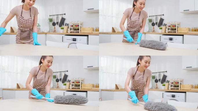 亚洲清洁服务女工在家厨房打扫卫生。漂亮的年轻管家清洁工穿围裙，用鸡毛掸子擦拭餐桌做家务或家务。