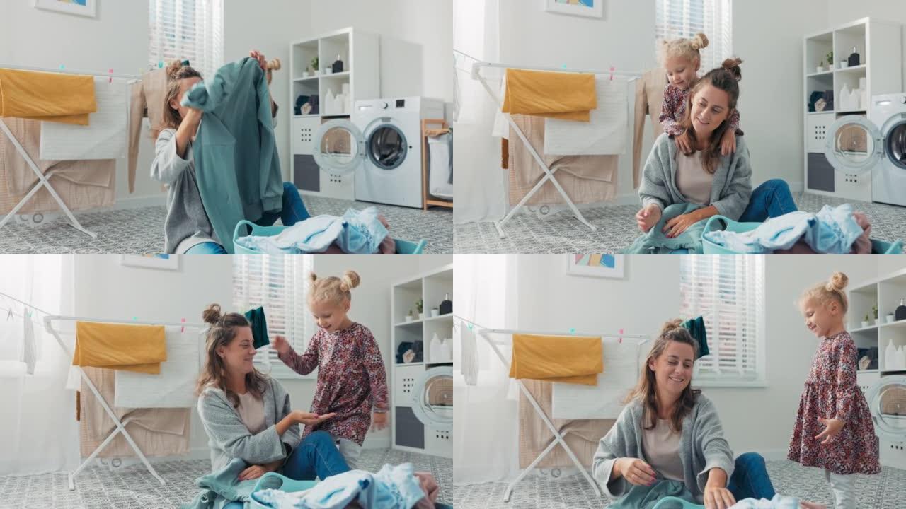 可爱的小女孩想和忙于家务的妈妈一起玩女人坐在洗衣房的浴室地板上整理洗衣服女儿从后面拥抱妈妈