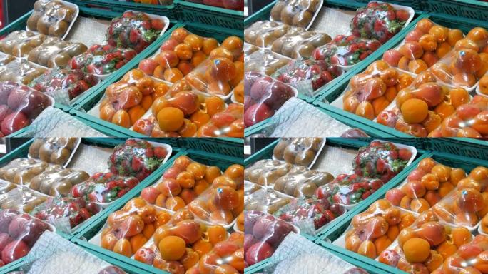 桃子，油桃，杏子，草莓，猕猴桃在特殊的玻璃纸布下在街头市场柜台上，免受灰尘和湿气的影响。