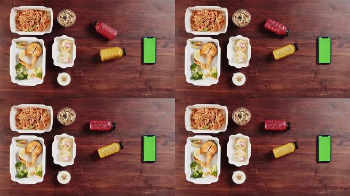食品配送应用程序，在木制桌子上的一次性容器中带走餐点。午餐盒的特写镜头，包括煮熟的部分，鱼，意大利面