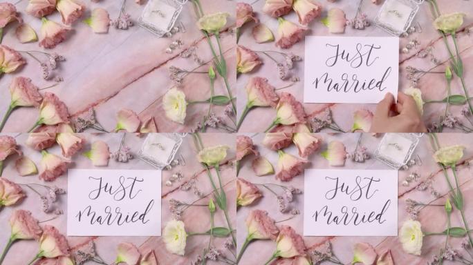 手将刚结婚的卡片放在粉红色花朵附近的大理石桌子上