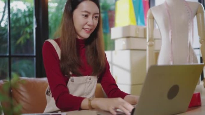 一名年轻的亚洲女性正在使用笔记本电脑与消费者交流，在她家的客厅里在线销售产品。