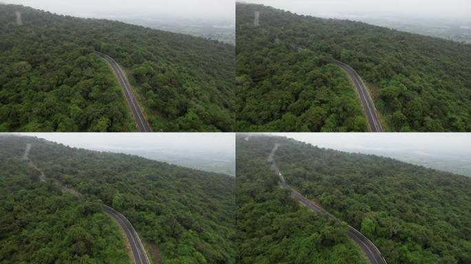 空中无人机电影拍摄的汽车和道路在早上下雨后越过山顶，有雾和绿色森林。