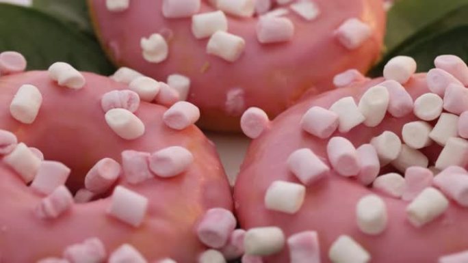 白色背景上的粉色糖霜甜甜圈。甜点。面包店和糖果。旋转特写镜头，美味可口的甜面包甜甜圈配五颜六色的糖霜