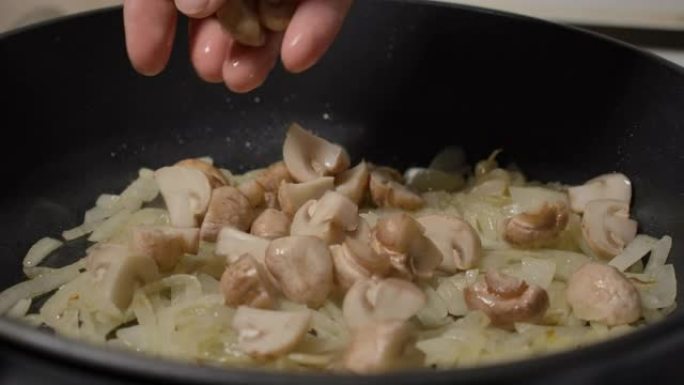 厨师用植物油中的洋葱炒蘑菇到煎锅做饭。慢动作烹饪慢动作人用橄榄油将洋葱炒蘑菇放入煎锅，特写镜头。宏观