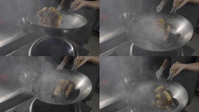 一家亚洲餐厅的厨师在厨房背景下的热煎锅里炸茄子。一名男子用热香料，大蒜和蔗糖糖浆在油中炸制蔬菜。慢动