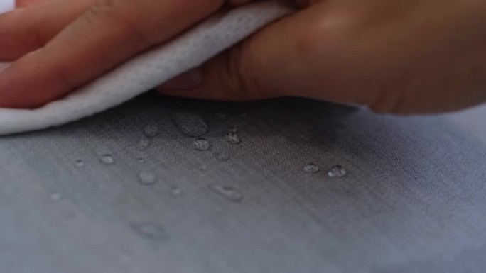 用手擦拭布上的水滴。防水纺织材料上的水滴。短景深。沙发上的防水织物