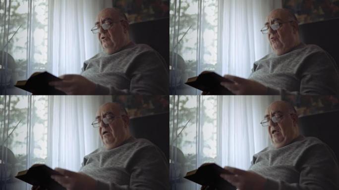 老人坐在沙发上，在窗户附近看书