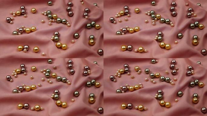 珍珠珠子不同颜色在桃色丝绸上滚动，背景，慢动作