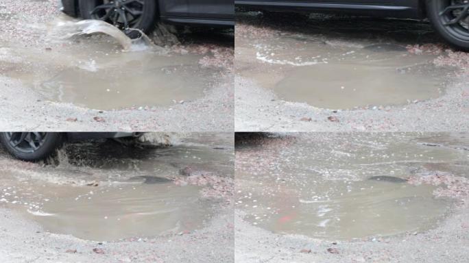 有过往汽车的柏油路面上充满水的坑洼。多雨的天气。白天下雨后，汽车在破碎的柏油路面上穿过水坑。雨滴和汽