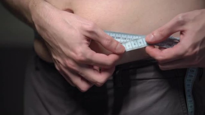 胖子。男人用卷尺量腰围。肚子、胃超重