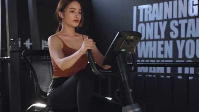 亚洲美女年轻成年白人妇女在体育俱乐部的自行车机上锻炼。有氧训练概念