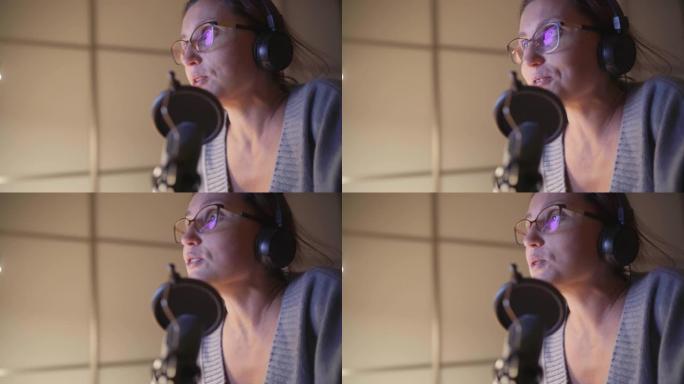 戴着耳机的中年女性博客作者使用带有pop过滤器的麦克风广播她的演讲。现代音频录音棚录音技术概念图像。
