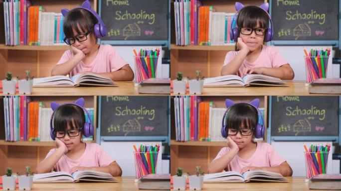 戴着耳机的可爱小女孩听有声读物桌上有英语学习书籍。学习英语与现代教育