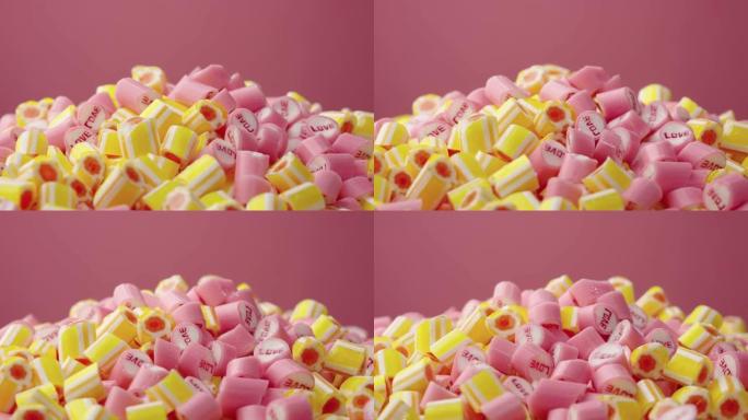 彩色条纹焦糖糖果，铭文爱在粉红色背景上旋转。粉色和黄色棒棒糖的混合特写。糖果店。节日或儿童生日的节日