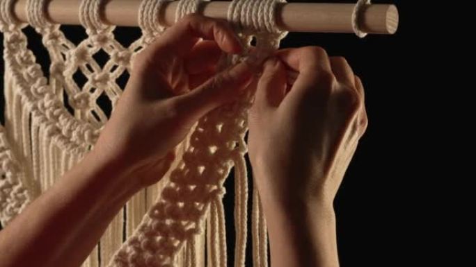 用天然白色棉线编织花边图案。女性的手编织结在黑色背景上创造蕾丝装饰。车间、纺织工艺品的创意过程。特写