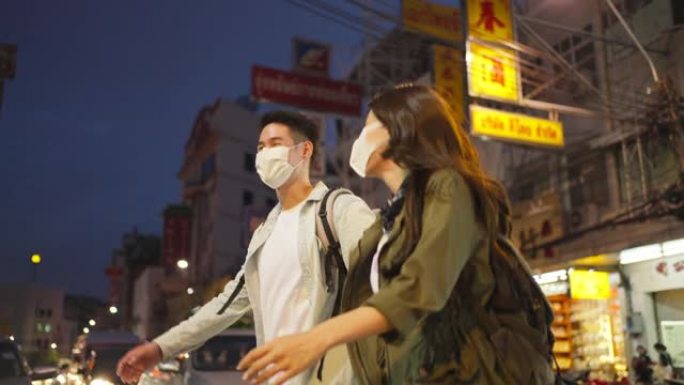 亚洲迷人的夫妇晚上在城市里度蜜月旅行。年轻的新婚男女背包客游客戴上口罩，以防止Covid19，一起度