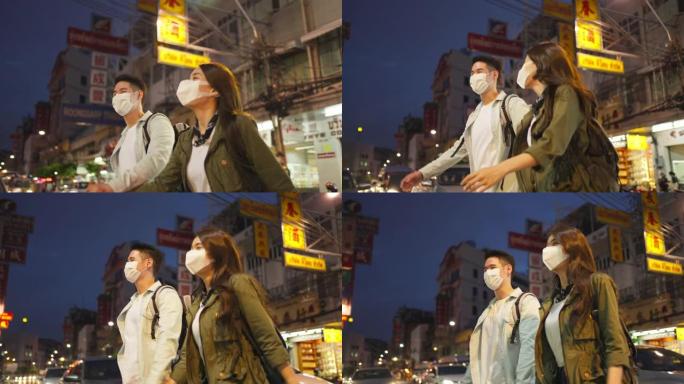 亚洲迷人的夫妇晚上在城市里度蜜月旅行。年轻的新婚男女背包客游客戴上口罩，以防止Covid19，一起度