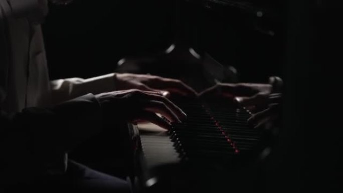 男性手在黑色背景的钢琴上演奏快速欢快的音乐。音乐家用手指触摸乐器的白色和黑色键，创造音乐旋律。特写。