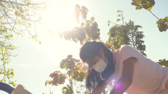 亚洲女孩戴着口罩在户外操场上玩太阳光，活跃和新的正常生活理念。