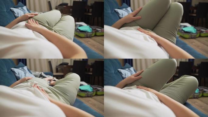 穿着白色t恤的女人躺在蓝色沙发上，用手托着肚子。用手抚摸胃，这样就不会受伤。月经，怀孕，腹泻，暴食。