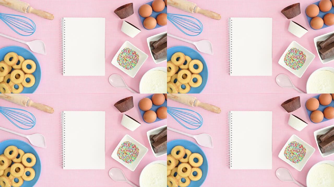 打开笔记本的食谱出现在带有饼干和烘焙食品的粉红色主题上。停止运动
