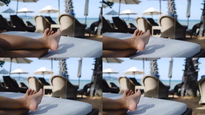 关闭躺在海上沙滩床椅子上的赤脚交叉腿