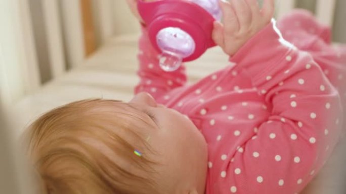 穿着粉色紧身衣的可爱快乐女婴在阳光明媚的早晨在室内喝水