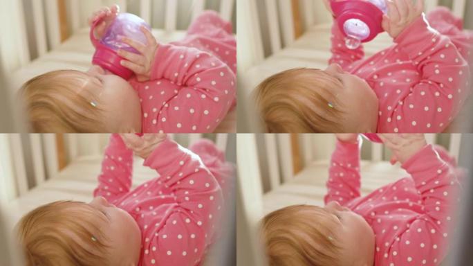 穿着粉色紧身衣的可爱快乐女婴在阳光明媚的早晨在室内喝水