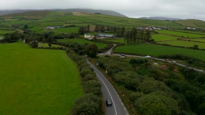 绿色农业景观的航拍画面。道路上通过急弯的车辆。远处被低云笼罩的小山。爱尔兰