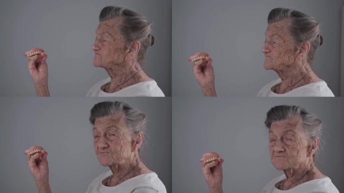 老年妇女脱下可移动的假牙，对着镜头和微笑。口腔护理概念、假牙和老年。老女性手中的全可摘义齿与白发工作